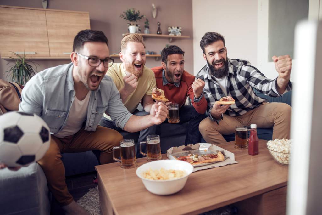 Group of friends watching soccer game on television, celebrating goal.