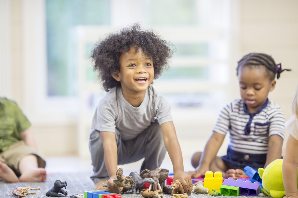 A group of toddlers are sitting on the floor playing with toy blocks and animals