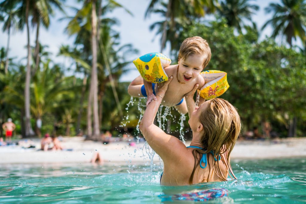 Cute kid having fun with his mother in the sea during their family summer vacation.