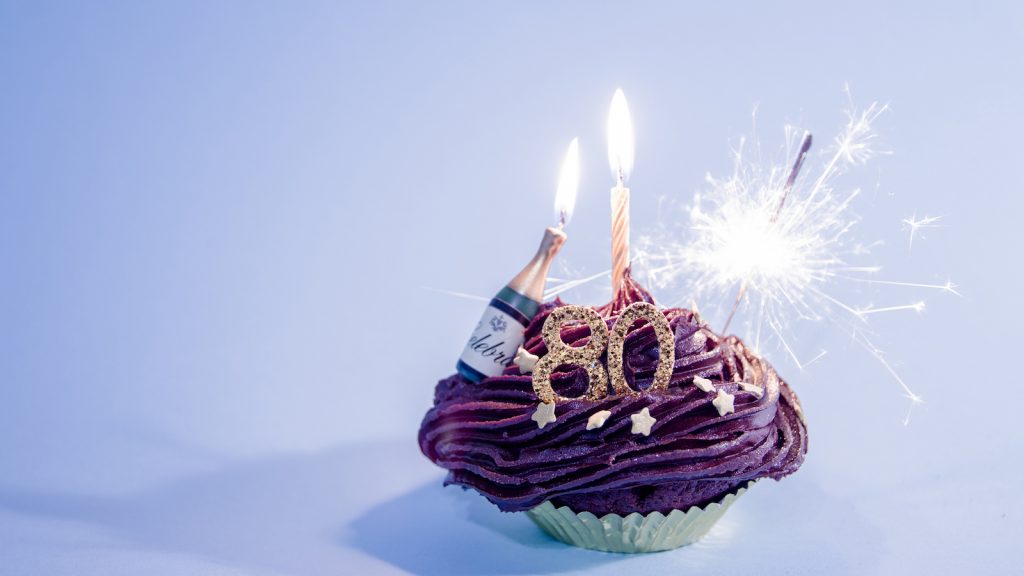 Chocolate birthday cupcake with gold numbers 80, and gold candle.