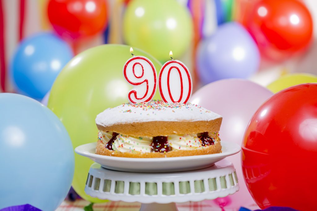 Cream filled sponge birthday cake with candles balloons and streams for a 90th birthday party.