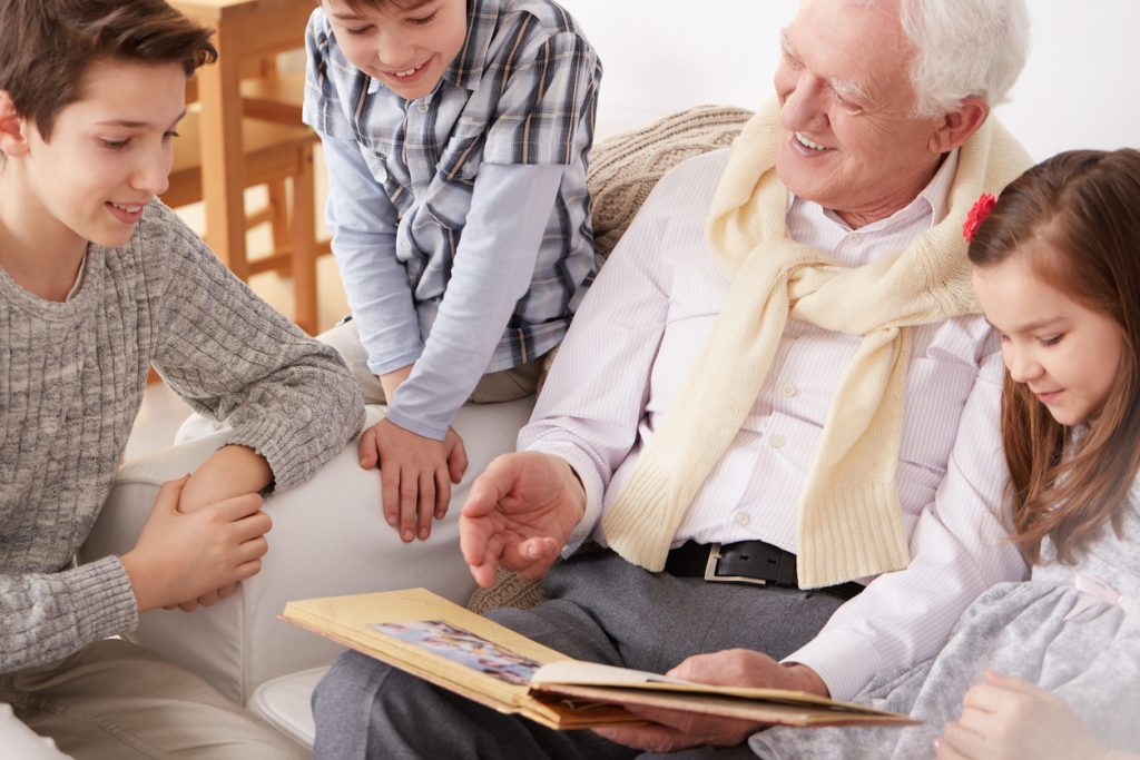 Happy children sitting on sofa with grandpa holding a photo album.