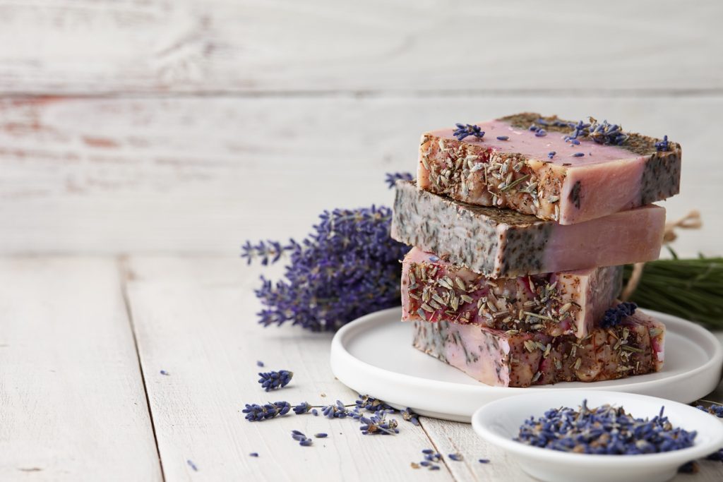 Lavender soap pile and flower blossoms on white wooden background.