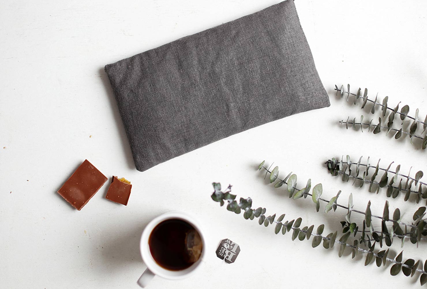 Gray heating pad next to mug of coffee and plant.