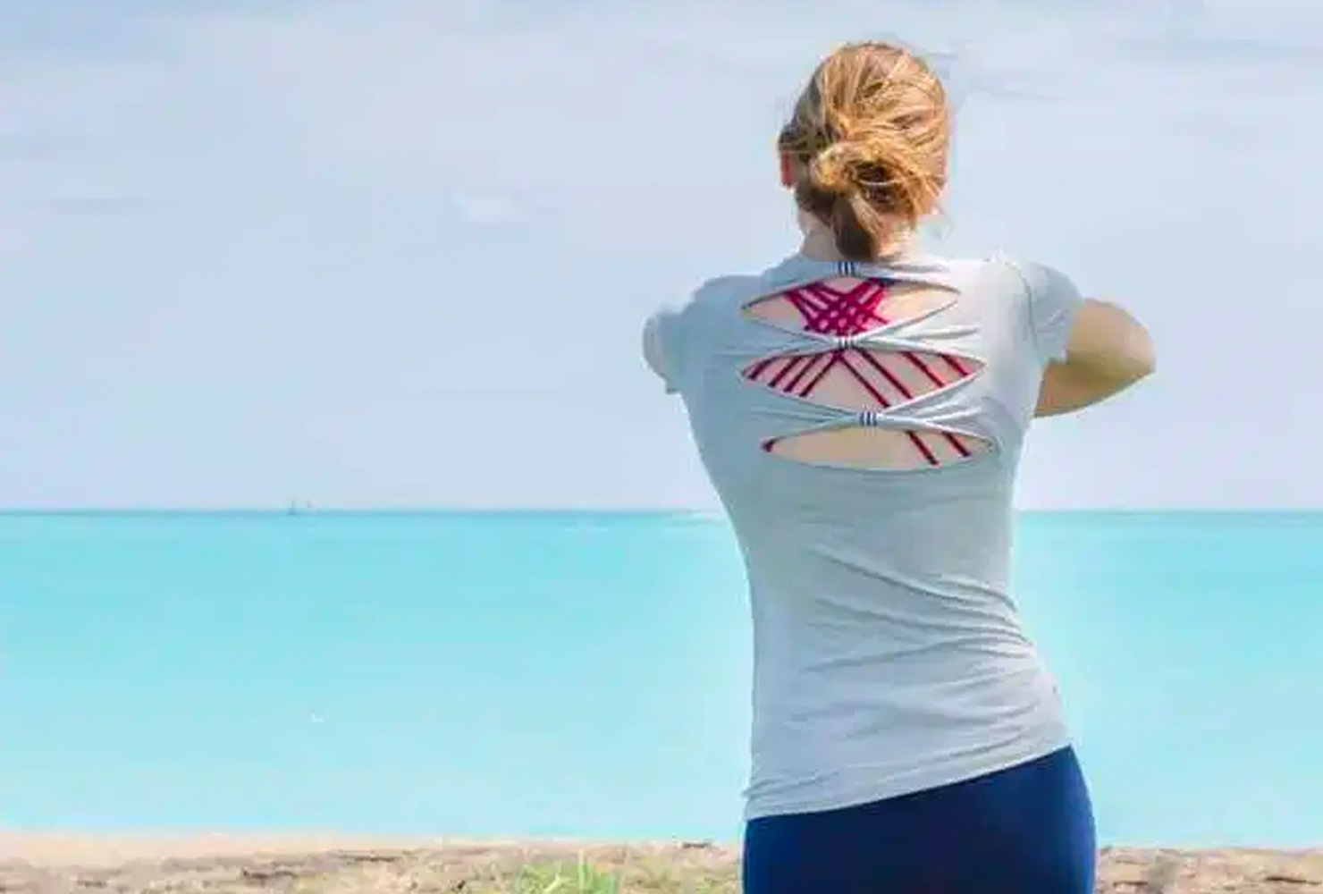 Woman in gray shirt with cutouts looking at the ocean.