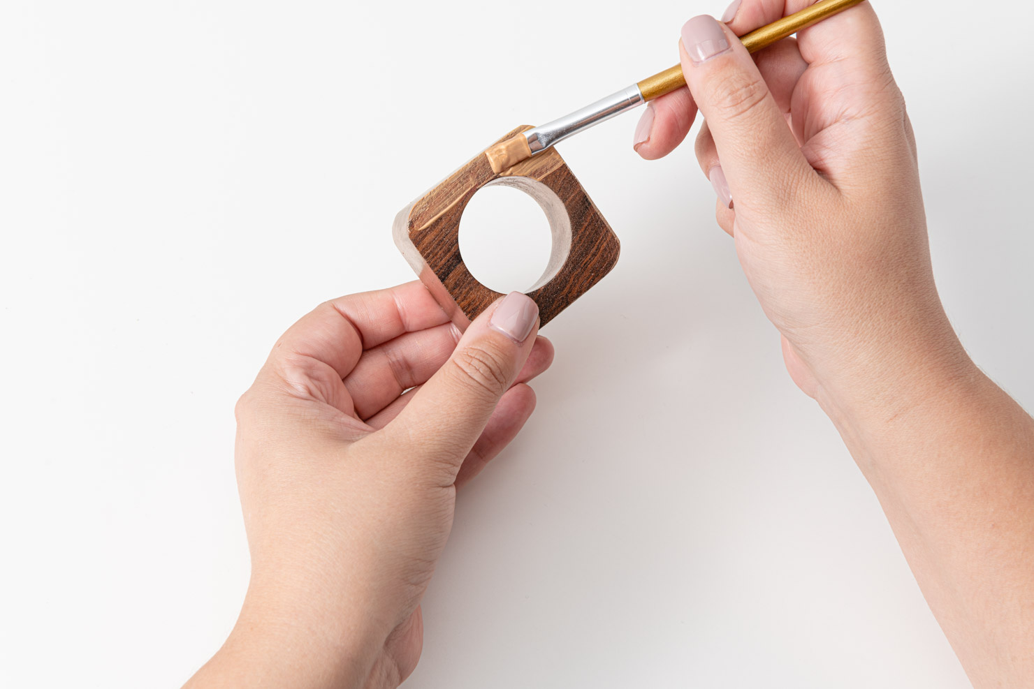 Someone painting a wooden napkin ring gold. 