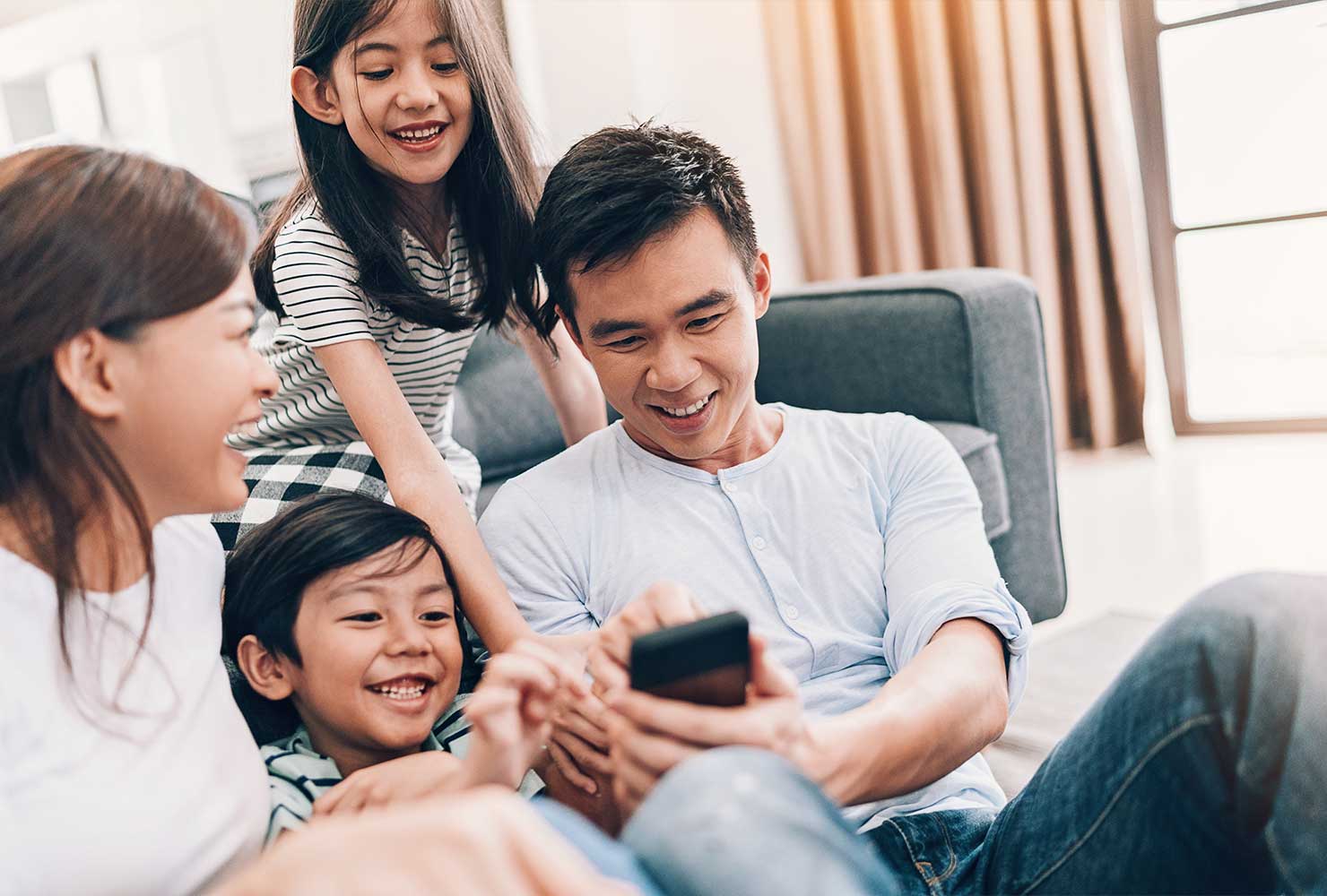 Mother father daughter and son gathered around cell phone laughing 