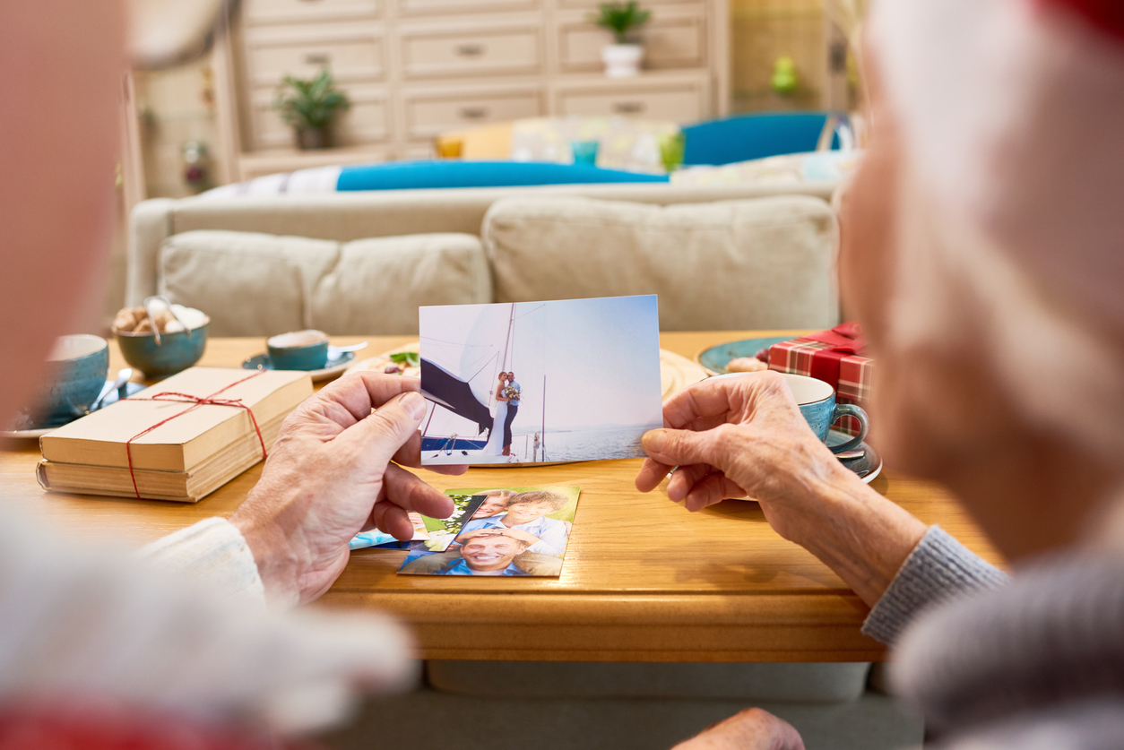 Back view of senior couple looking at family photographs remem bering children during Christmas holidays